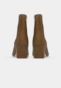 Um par de botas de tornozelo em camurça castanha com saltos quadrados, mostrado por trás em fundo branco.