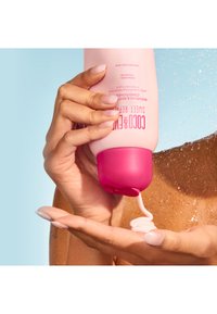 Rosa flaska med reparerande och återställande balsam med pumplock. Krämig vit produkt som pressas ut i en hand, något glänsande textur.