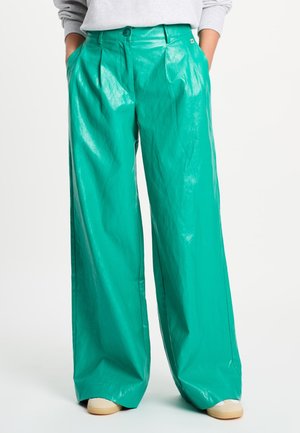 Petrolkleurige wijde broek met plooien aan de voorkant, gedragen met een lichtgrijze trui en beige sneakers op een witte achtergrond.