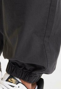Zwarte joggings met een gestructureerde stof, voorzien van een elastische tailleband en boorden, gecombineerd met wit-zwart sneakers.