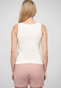 Un débardeur blanc à côtes vu de dos, associé à un short rose doux avec un ourlet roulé. Texture lisse, design ajusté.