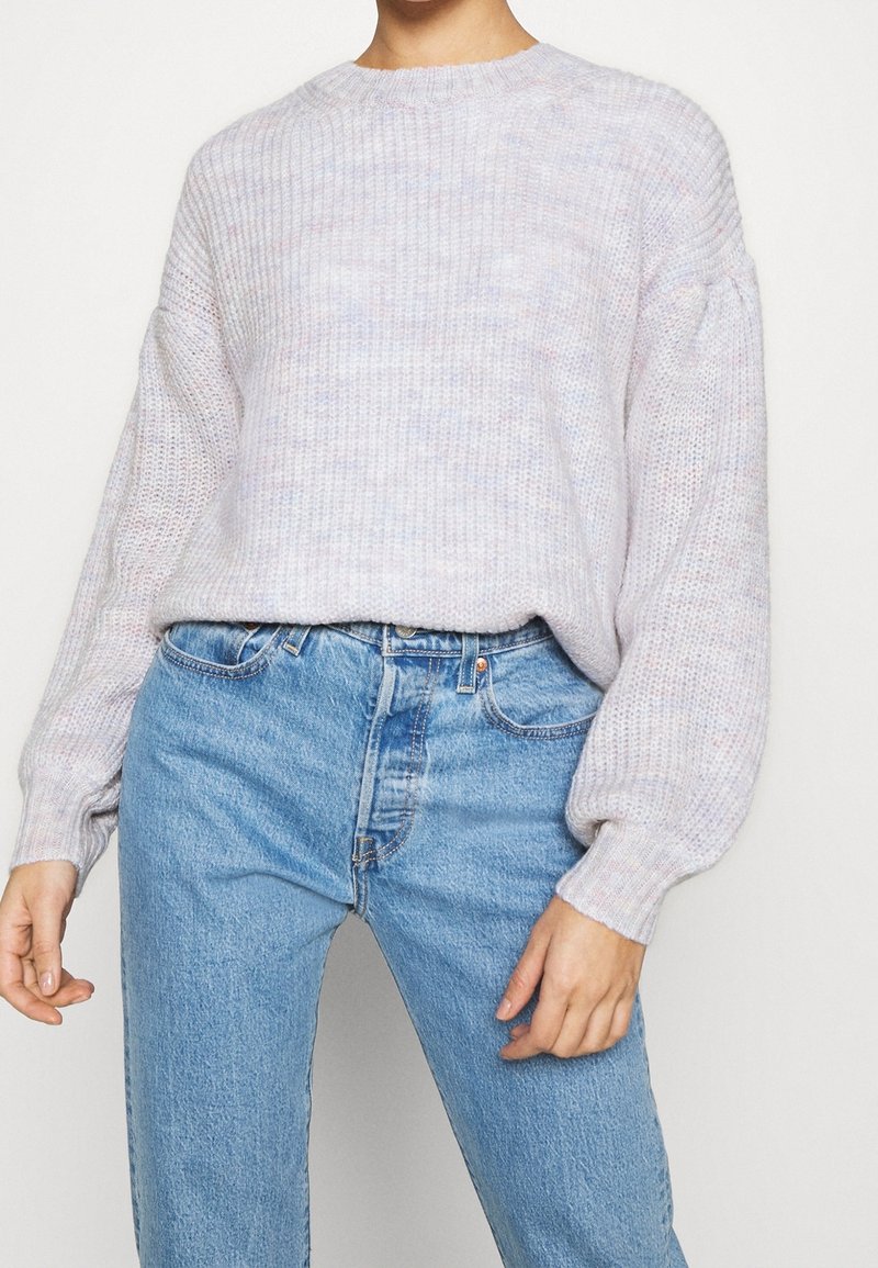 Femme portant un pull en maille violet clair à manches ballon, rentré dans un jean en denim bleu clair taille haute.