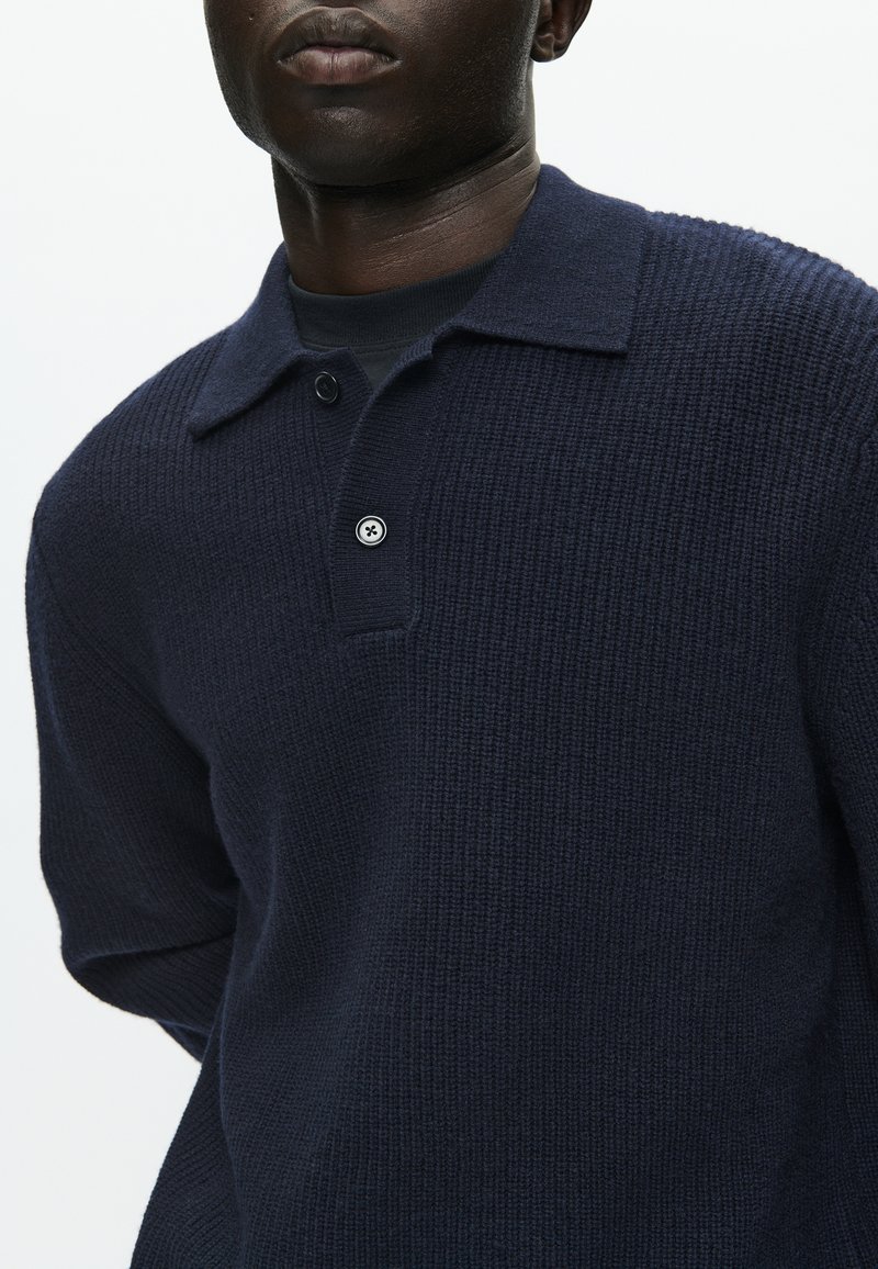 Maglione polo in maglia blu navy con superficie strutturata, colletto corto e chiusura con un solo bottone al collo. Vestibilità classica.