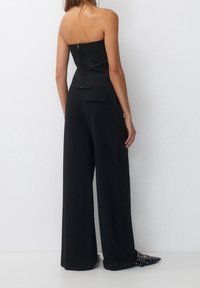 Top noir sans bretelles avec un corsage ajusté et une fermeture éclair dans le dos, associé à un pantalon noir à jambes larges et des chaussures noires à talons pointus.