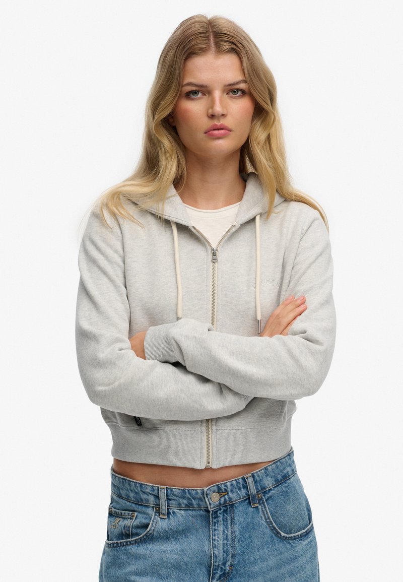 Lichtgrijze hoodie met ritssluiting, capuchon met trekkoord, geribbelde manchetten en zoom. Gecombineerd met een high-waisted blauwe spijkerbroek. Eenvoudig ontwerp.