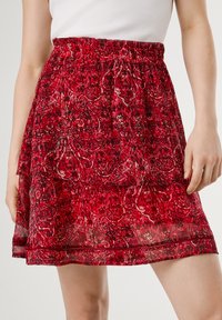 Jupe à motifs rouges avec une taille élastique froncée, présentant un design en couches et un tissu léger et fluide.