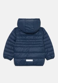 Veste à capuche matelassée bleu marine, texturée, avec des poignets élastiques. Comprend un détail réfléchissant au bas du dos.