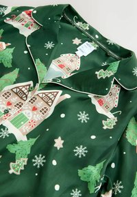 Green pajama set with festive print featuring houses, trees, and snowflakes. Soft fabric, classic collar, and white piping accents.