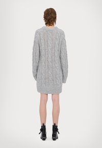 Rochie tricotată gri cu model cablu, cu mâneci lungi, tiv ribbit și design cu decupaje. Purtați cu cizme negre până la gleznă cu fundițe decorative.