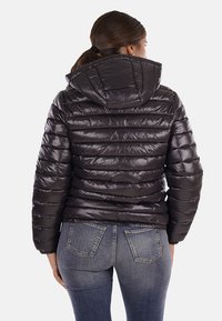 Giacca nera imbottita con cappuccio, caratterizzata da un design trapuntato e una finitura lucida. Abbinata a jeans in denim blu con vestibilità classica.