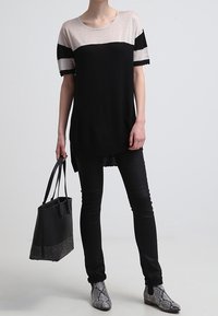 Haut coloré en noir et beige avec des manches courtes, associé à un pantalon noir ajusté et des bottines à imprimé serpent gris. Accompagné d'un sac noir.