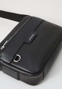 Borsa a tracolla in pelle nera con superficie testurizzata, chiusura con zip frontale, accessori in argento e etichetta con logo. Inclusa una tracolla regolabile.
