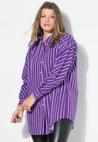 Camicia a maniche lunghe di colore viola con righe bianche verticali, dotata di taschino sul petto. Presenta un orlo curvo e una texture del tessuto liscia.