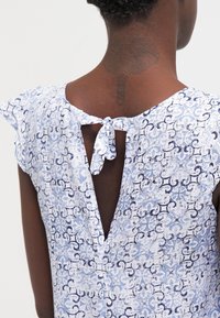 Modré a bílé šaty se vzorem, s jemnými rukávy, zadním výstřihem ve tvaru klíče a zavazováním na krku. Lehce texturovaná látka.