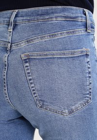 Vaqueros de denim azul claro con una silueta ajustada. Presentan dos bolsillos traseros con detalles de costura y una cintura de altura media.