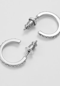 Pendientes de aro de plata con un acabado pulido, que presentan pequeñas piedras brillantes transparentes a lo largo del borde y un cierre trasero seguro.