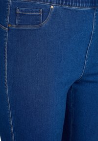 Blue denim jeans with a slightly textured surface, featuring visible stitching, a small pocket, and gold-tone hardware accents.