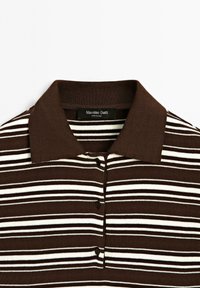Brun og creme stribet polo shirt med en ribbet tekstur, der har krave, tre-knap placket og et mærke ved halsudskæringen.