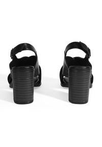 Zwarte leren sandalen met blokhak, een enkelbandje, open teen en een ribbelontwerp op de hak. De zool heeft een gladde textuur.