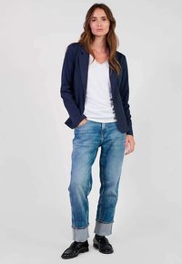 Blazer blu navy, maglietta bianca a scollo a V, jeans azzurri chiari risvoltati e scarpe nere. Tessuto liscio, design su misura e vestibilità classica.