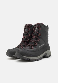 Bottes noires imperméables avec une finition texturée, bout renforcé, lacets rouges et semelles robustes pour une meilleure traction. Présente le logo Columbia sur le côté.