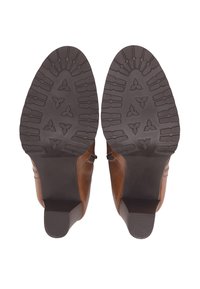 Hnědé kožené kotníkové boty s texturovanou gumovou podrážkou se zigzagovým vzorem a nízkým podpatkem. Boční akcenty zvýrazňují design.