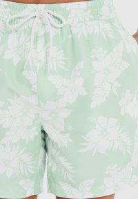 Vaaleanvihreät uimapuvut, joissa on valkoinen kukkakuosi. Varustettu joustavalla vyötärökaistalla, jossa on nyöritys sekä pienillä sivutaskuilla.