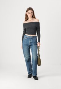 Top cropped preto sem ombros com textura canelada, emparelhado com jeans de cintura alta azul desbotada. Modelo segura uma bolsa de ombro verde.
