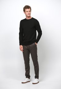Schwarzer Strickpullover mit langen Ärmeln, schlanke braune Hose und weiße Sneakers. Lässiges Outfit mit glatter Textur und schlichtem Design.