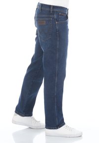 Jeans de mezclilla azul oscuro con un diseño de pierna recta, bolsillos traseros con un patrón de costura distintivo y una etiqueta de cuero en la cinturilla.