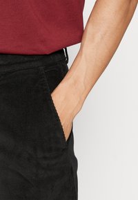 Svarta corduroybyxor med en strukturerad yta, med en sidoficka och en åtsittande midja, tillsammans med en vinröd t-shirt.