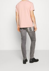 Light pink short-sleeve t-shirt paired with fitted gray jeans. The jeans feature distressed accents and back pockets. Black ankle boots complete the look.