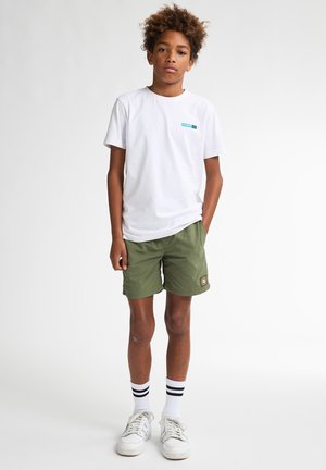Witte T-shirt met korte mouwen en teal logo, groene shorts, zwart-wit gestreepte sokken en witte sneakers. Casual zomertenue.