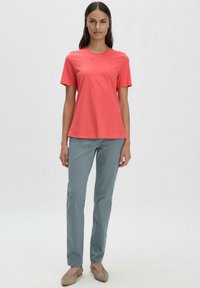 Korallinen lyhythihainen T-paita pyöreällä kaula-aukolla, yhdistettynä vaalean teal-värisiin suoriin housuihin ja beigellä kengillä. Sileä puuvillakangas.