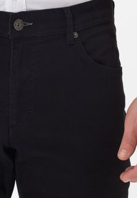 Black cotton pants featuring a standard fit, front pockets, a smooth texture, and a metal button closure at the waistband.