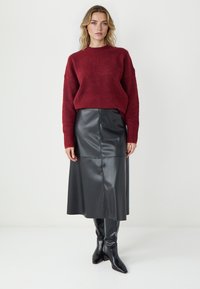 Bordeaux gebreid sweater met lange mouwen, gecombineerd met een zwarte leren midi rok en zwart leren laarzen met hoge hakken tot de knie. Glad texturen contrasteren.