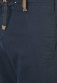 Pantaloni din bumbac ușor, de culoare albastru marin, cu un finisaj texturat, dotati cu un șnur de ajustare și cu o etichetă din piele bej. Designul include buzunare laterale.