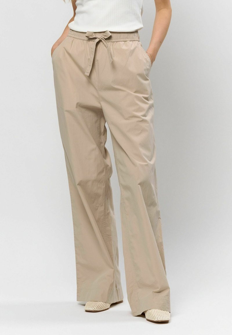 Béžové široké nohavice vyrobené z ľahkého materiálu, s elastickým pásom na šnurovanie, bočnými vreckami a hladkou textúrou.