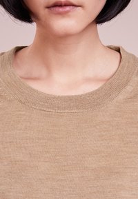 Beżowy sweter dzianinowy z szerokim okrągłym dekoltem, o miękkiej, gładkiej fakturze i subtelnej wariacji odcieni.