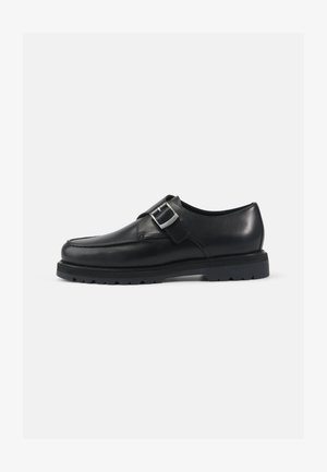 Chaussure en cuir noir avec une finition lisse, une forme arrondie et un détail de boucle en argent. Semelle épaisse noire avec traction.