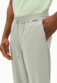 Lichtgroene joggerbroek met een elastische tailleband met trekkoord, zijzakken en een label op de linker heup. De stof lijkt glad te zijn.