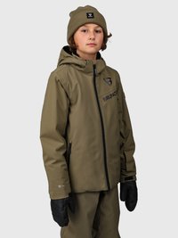 Bambino vestito con giacca e pantaloni invernali verde oliva, guanti neri e cappello di lana verde oliva, in piedi su uno sfondo chiaro e semplice.
