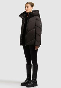 Giacca a vento nera con design a zigzag, grande colletto e zip laterale. Abbinata a leggings neri e stivali platform al ginocchio.