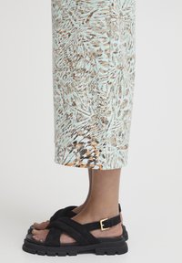Sandales en suède noir avec de larges straps et une boucle dorée. Les motifs du tissu présentent des tons de bleu clair, marron et orange.