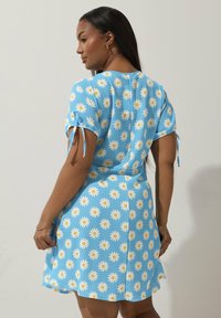 Sininen lyhyt mekko, jossa on valkoiset kamomillakuviot, lyhyet hihat siteillä, pehmeä rakenne ja levenevä hameen muoto.