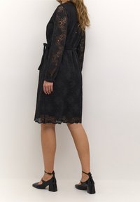 Svart spetklänning med lång ärm, midjebälte och scallopkant. Buren med svarta klackskor med ankelsnören.