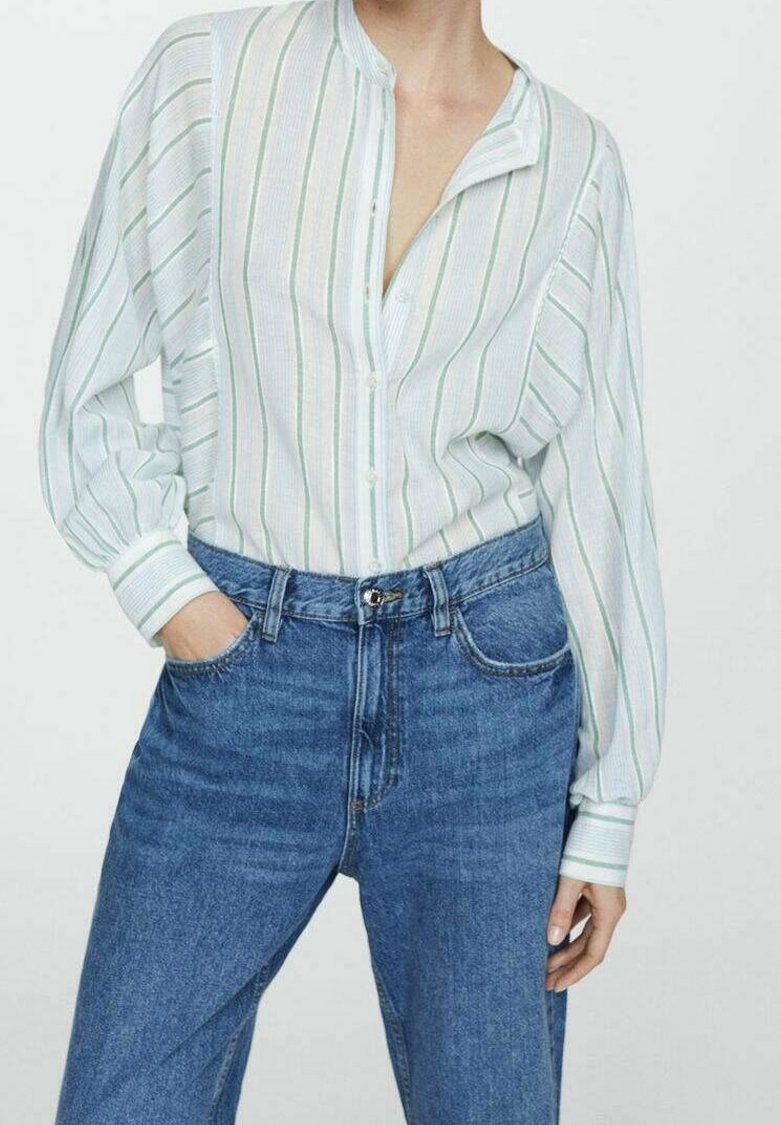 Chemise boutonnée bleu clair à rayures avec col mandarin, présentant des rayures verticales vertes et blanches, associée à un jean bleu taille haute.
