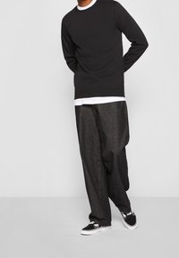 Felpa nera abbinata a pantaloni larghi grigi scuri, con una maglietta bianca sotto e sneakers nere con dettagli bianchi.