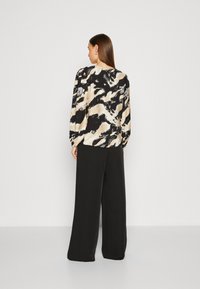 Blusa a maniche lunghe con un motivo astratto in nero, beige e avorio; presenta un colletto arrotondato e maniche leggermente gonfie. Abbinata a pantaloni neri.