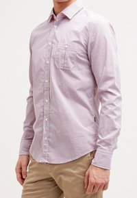 Camisa de botones a cuadros rojos y blancos con mangas largas, bolsillo delantero y cuello clásico, confeccionada en tela suave y ligera.